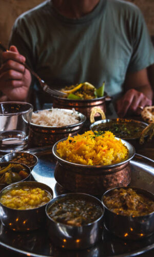 about2 Man (unrecognizable) eating traditional food in an Indian restaurant. Vegetarian Thali set on the tray, chicken curry, rice, naan and other delicious dishes on the table. Foodie travel background.
